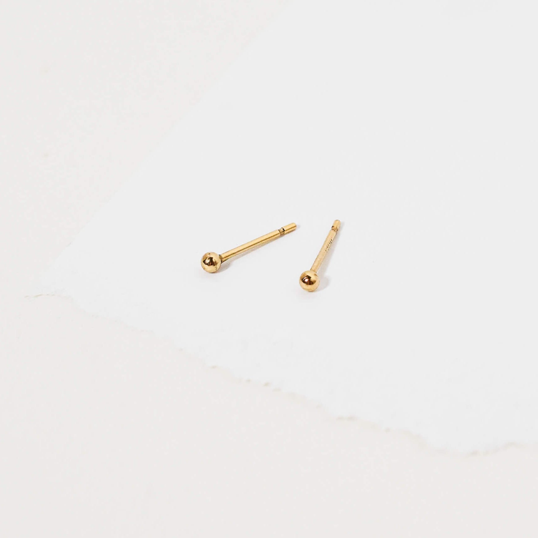 A pair of small gold stud earrings with round ball tops, displayed on a clean white surface.