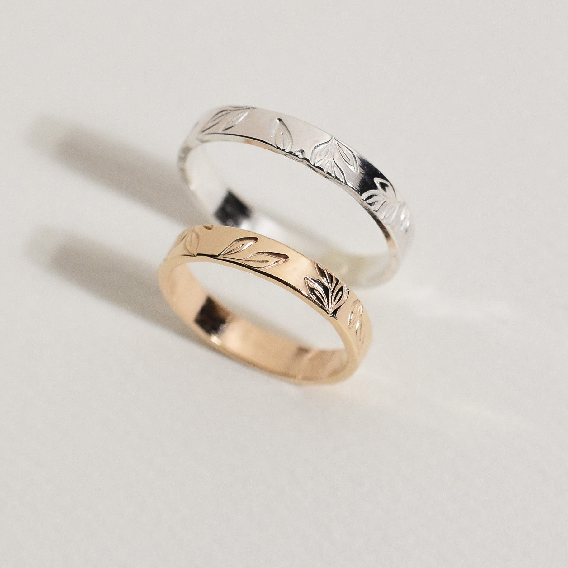Two leaf pattern engraved rings, one silver-toned and one rose gold-toned, displayed on a clean off-white background.