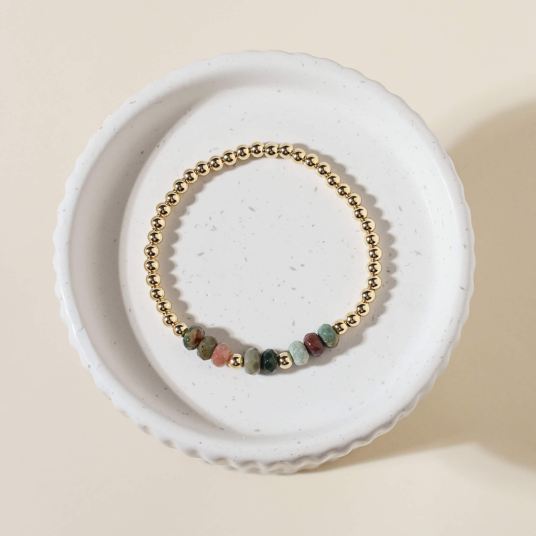 A gold-colored bracelet with faceted agate gemstone beads and gold-fill seamless beads, displayed on a white stand.